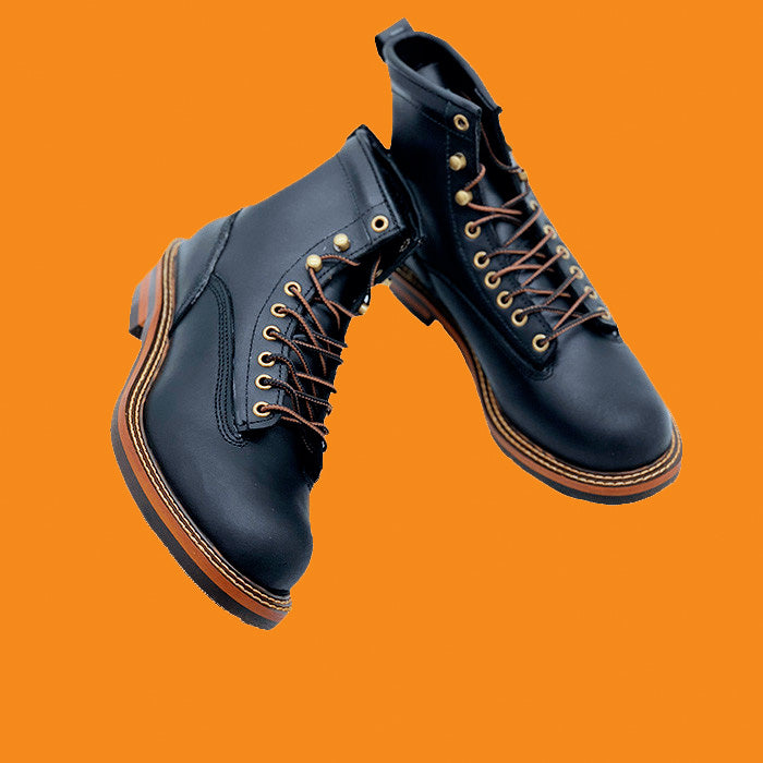 Black leather boots with brown laces on an orange background
