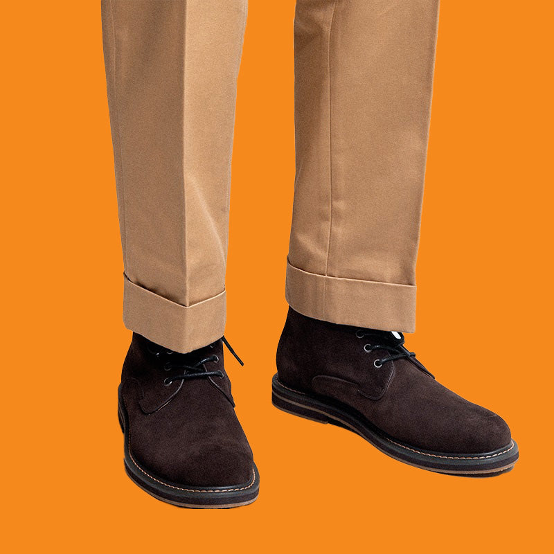 Brown suede shoes worn with beige pants against an orange background
