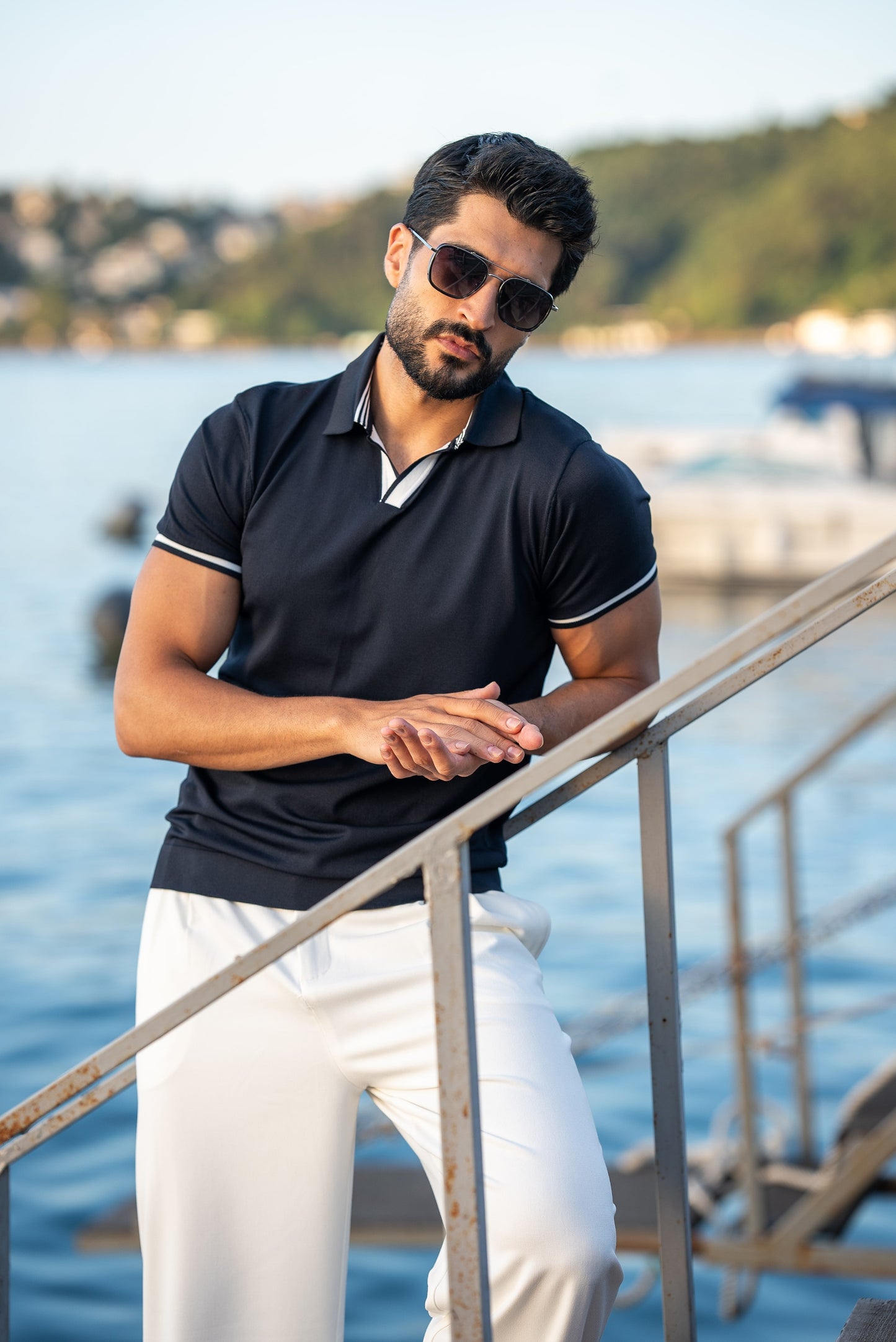 Man wearing sunglasses and a black polo shirt by a waterfront