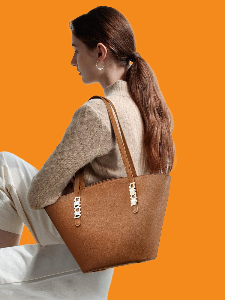 Woman holding a brown leather handbag against an orange background