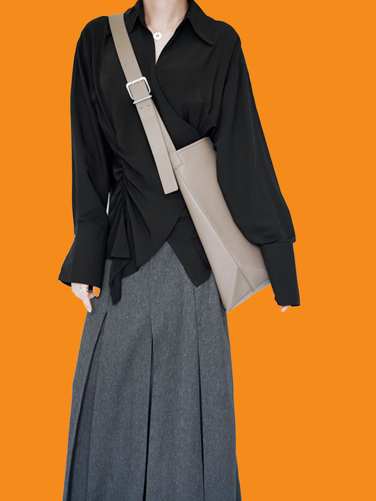 Person wearing a black shirt and gray pants with a beige crossbody bag on an orange background