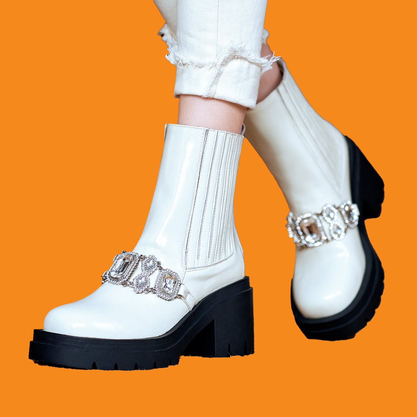 White ankle boots with black soles and silver embellishments on a bright orange background