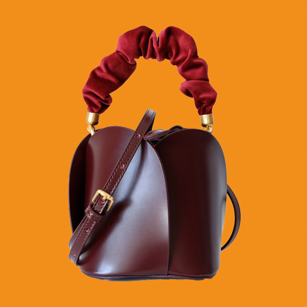 Brown leather handbag with red velvet handles on an orange background