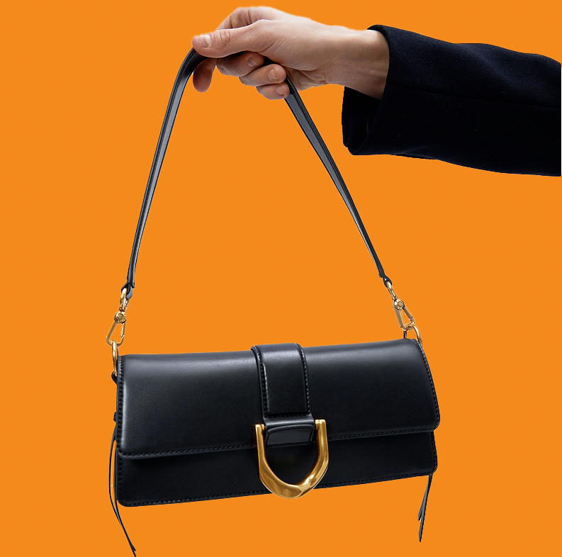 Black handbag with gold accents held by a hand against an orange background