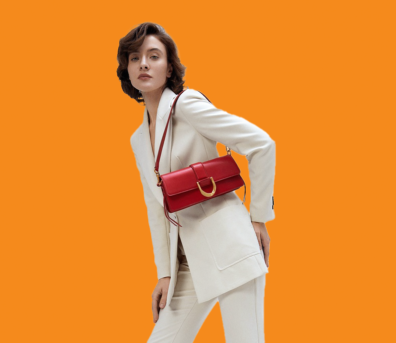 Woman in a white suit holding a red handbag against an orange background