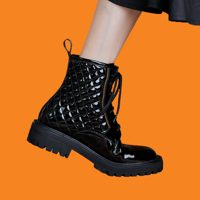 Black lace-up boot on a person's foot against an orange background