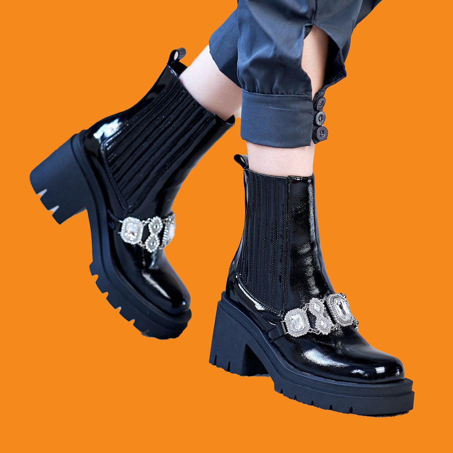 Black shiny boots with decorative elements on an orange background