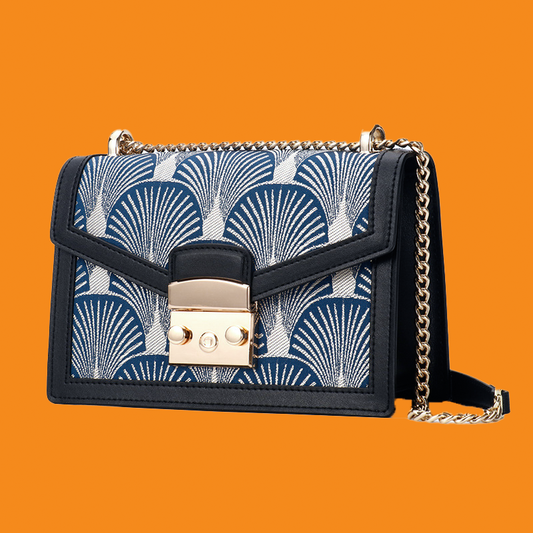Handbag with blue patterned flap and gold chain strap on orange background