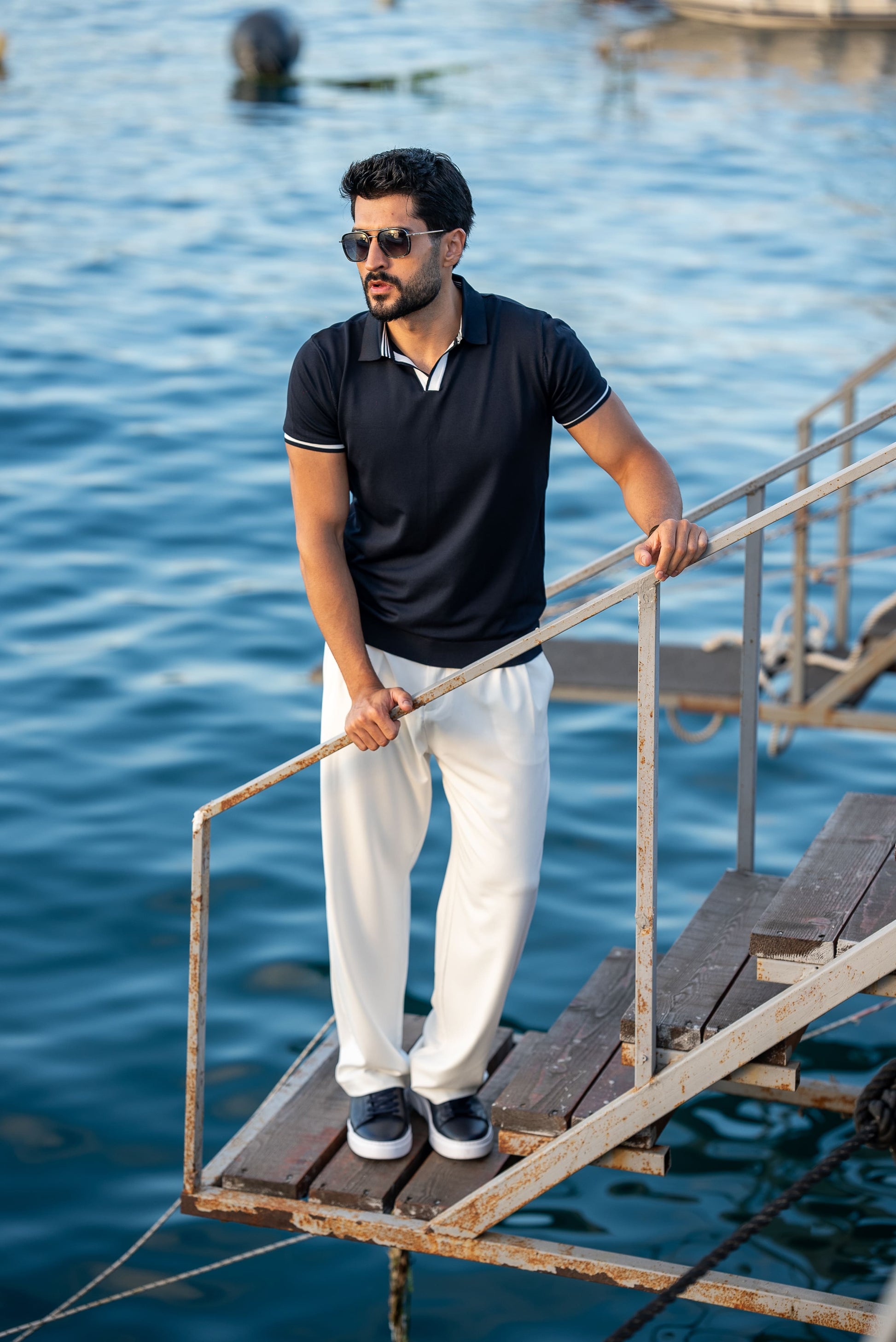 Man standing on a wooden platform by the water wearing sunglasses and a dark polo shirt.
