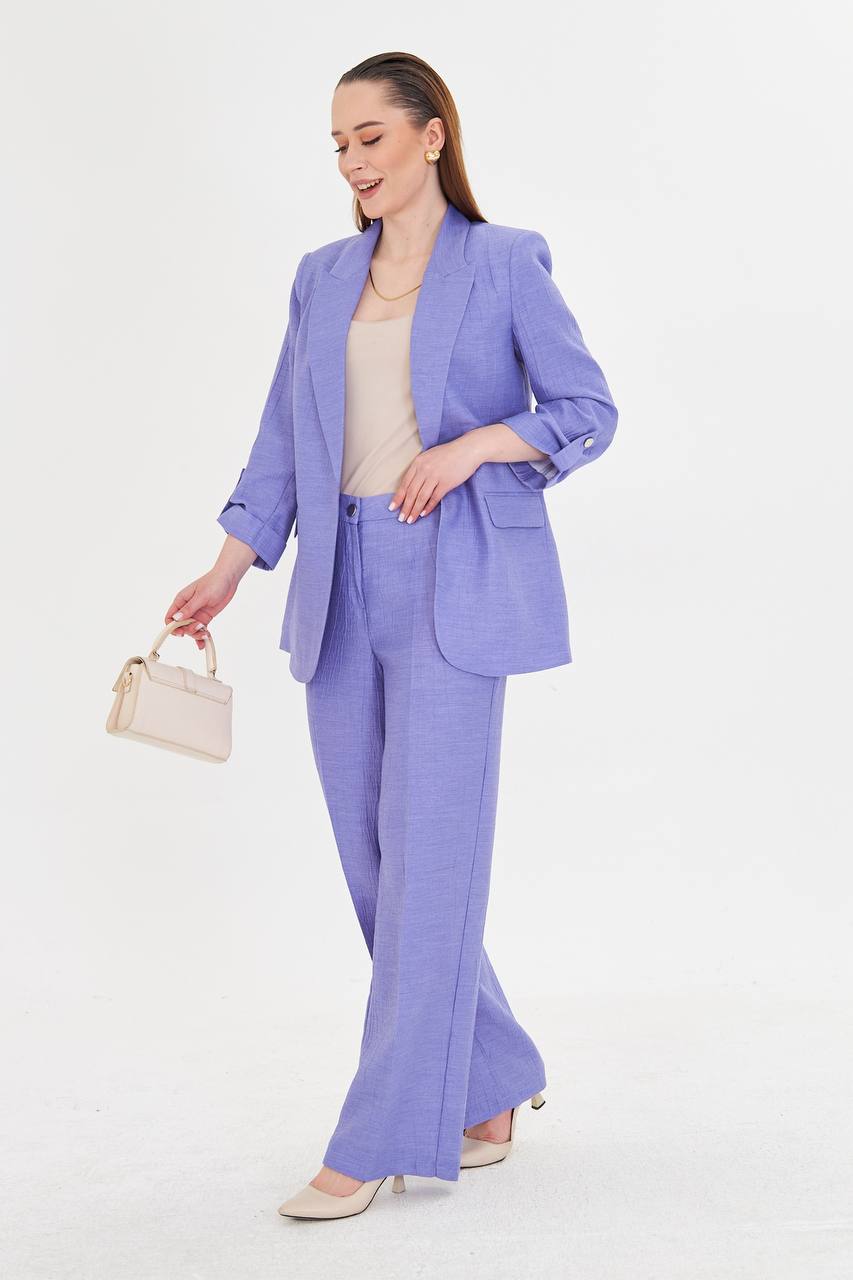 Woman wearing a light purple suit with a beige top and handbag on a white background
