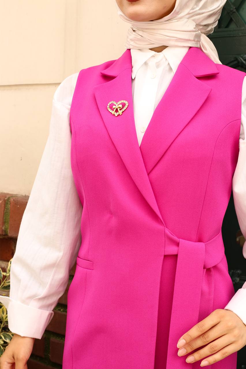 Person wearing a bright pink vest with a heart-shaped brooch, white shirt, and hijab.
