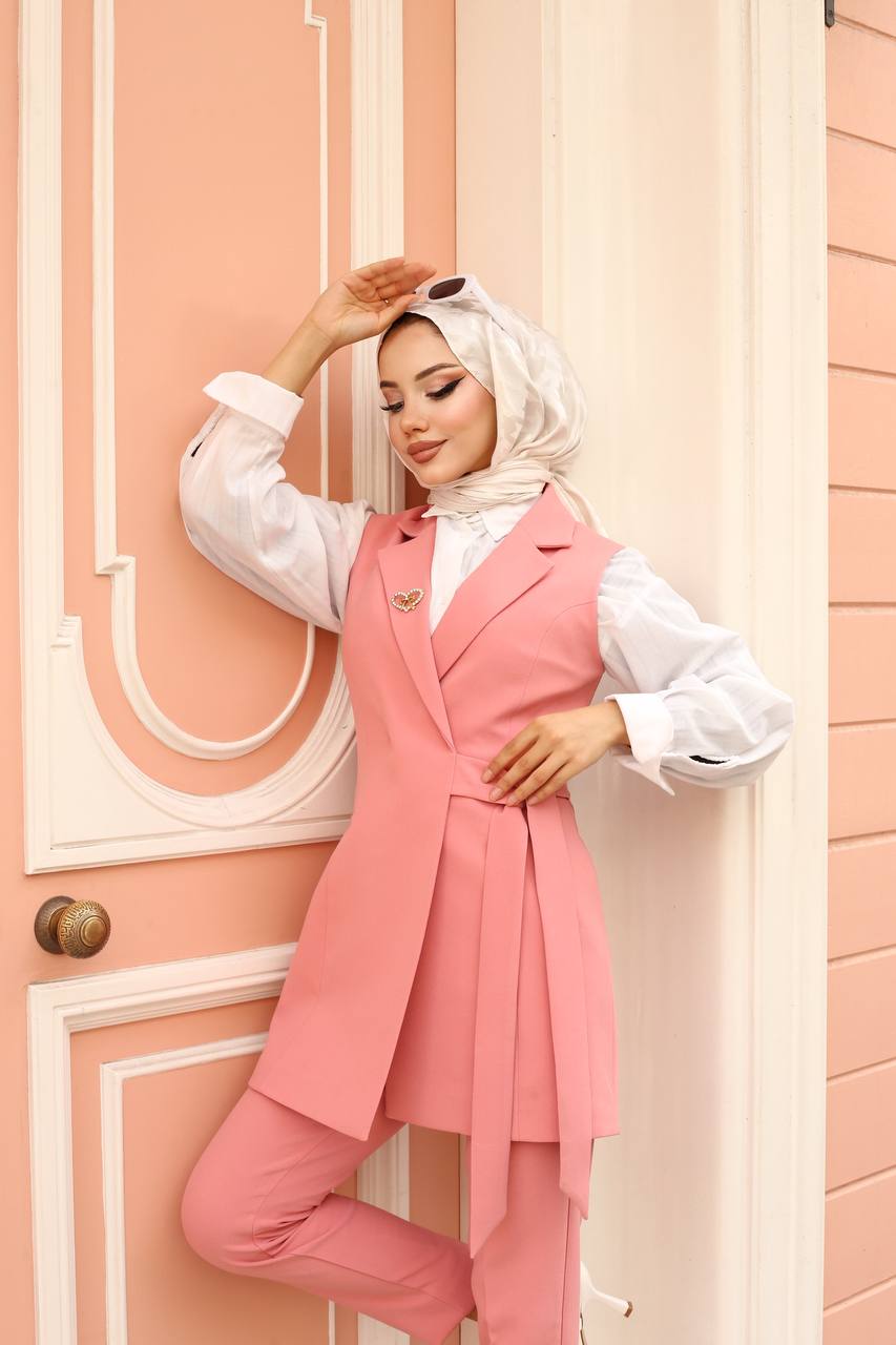 Woman wearing a pink outfit with a white hijab against a pink wall.