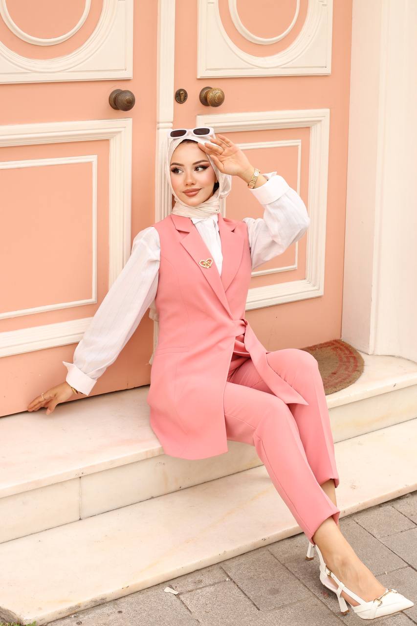 Woman in a pink outfit sitting on steps with a decorative pink wall in the background