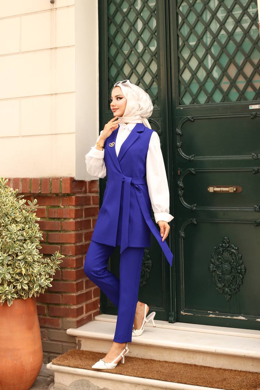 Woman in a blue vest and pants standing on steps in front of a green door.