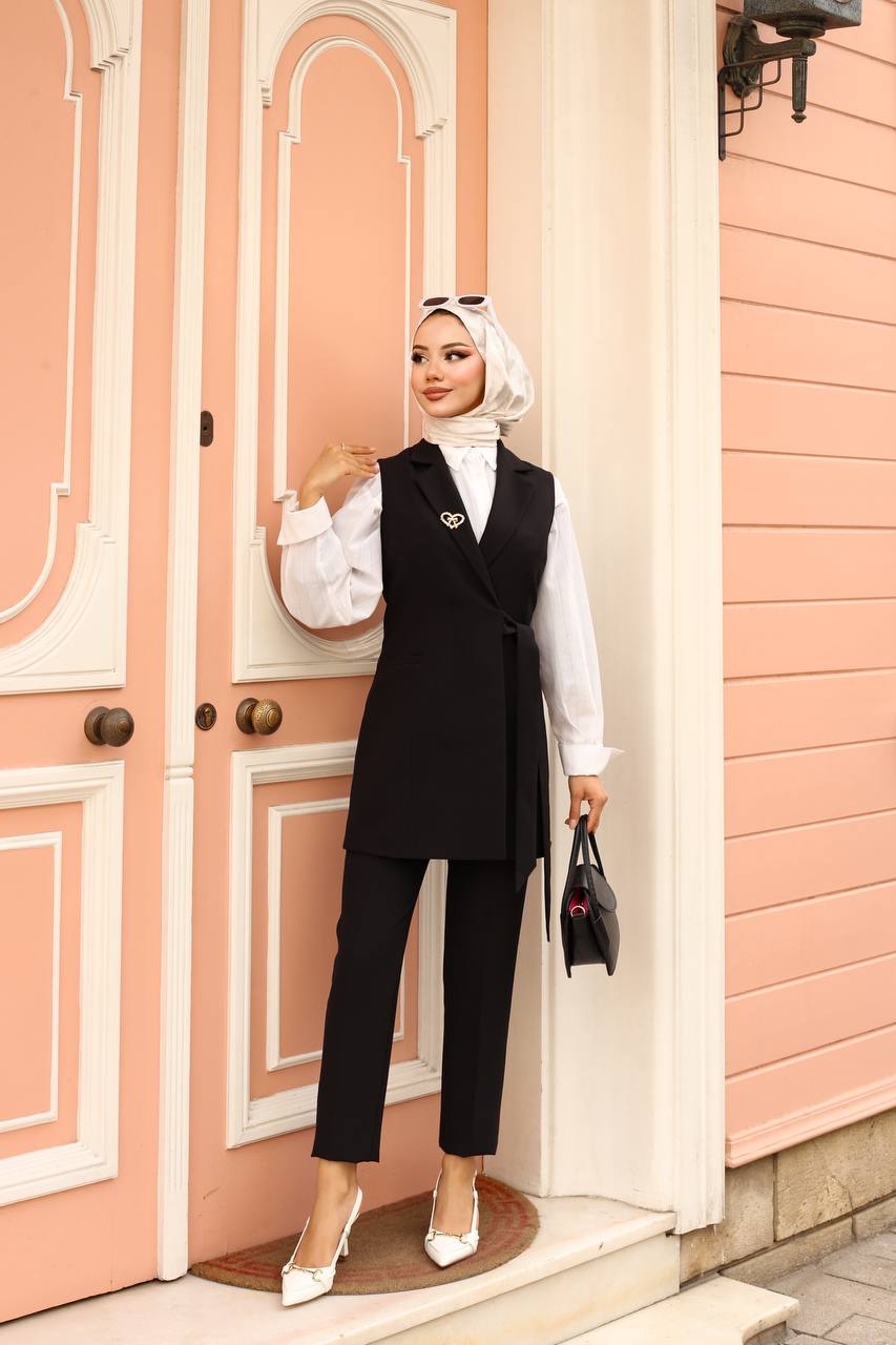 Woman in a black vest and pants standing in front of a pink door.
