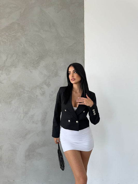 Woman wearing a black blazer and white skirt against a textured wall.