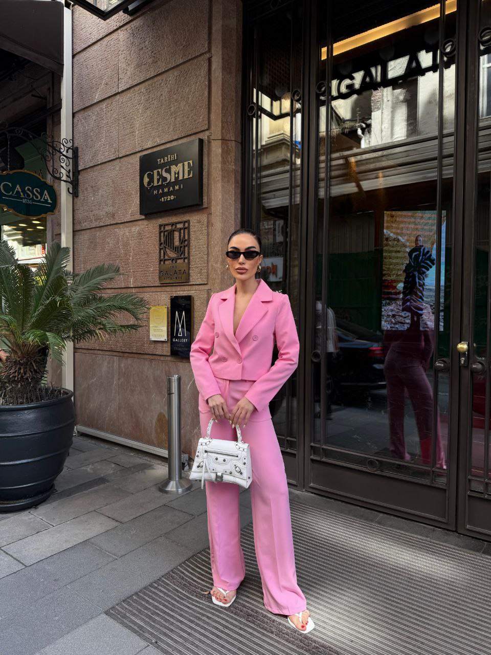 Woman in a pink suit standing in front of a building entrance.