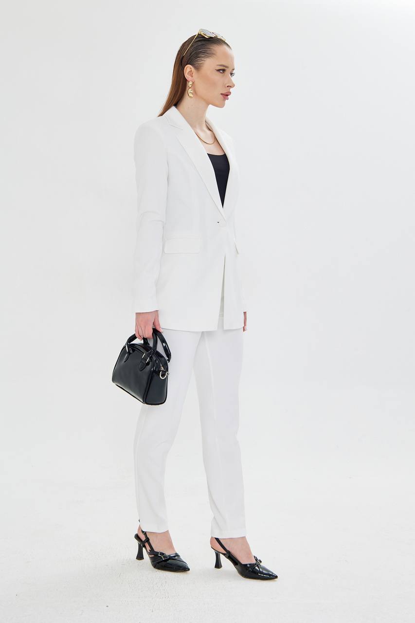 Woman wearing a white suit with black shoes and a black handbag on a white background