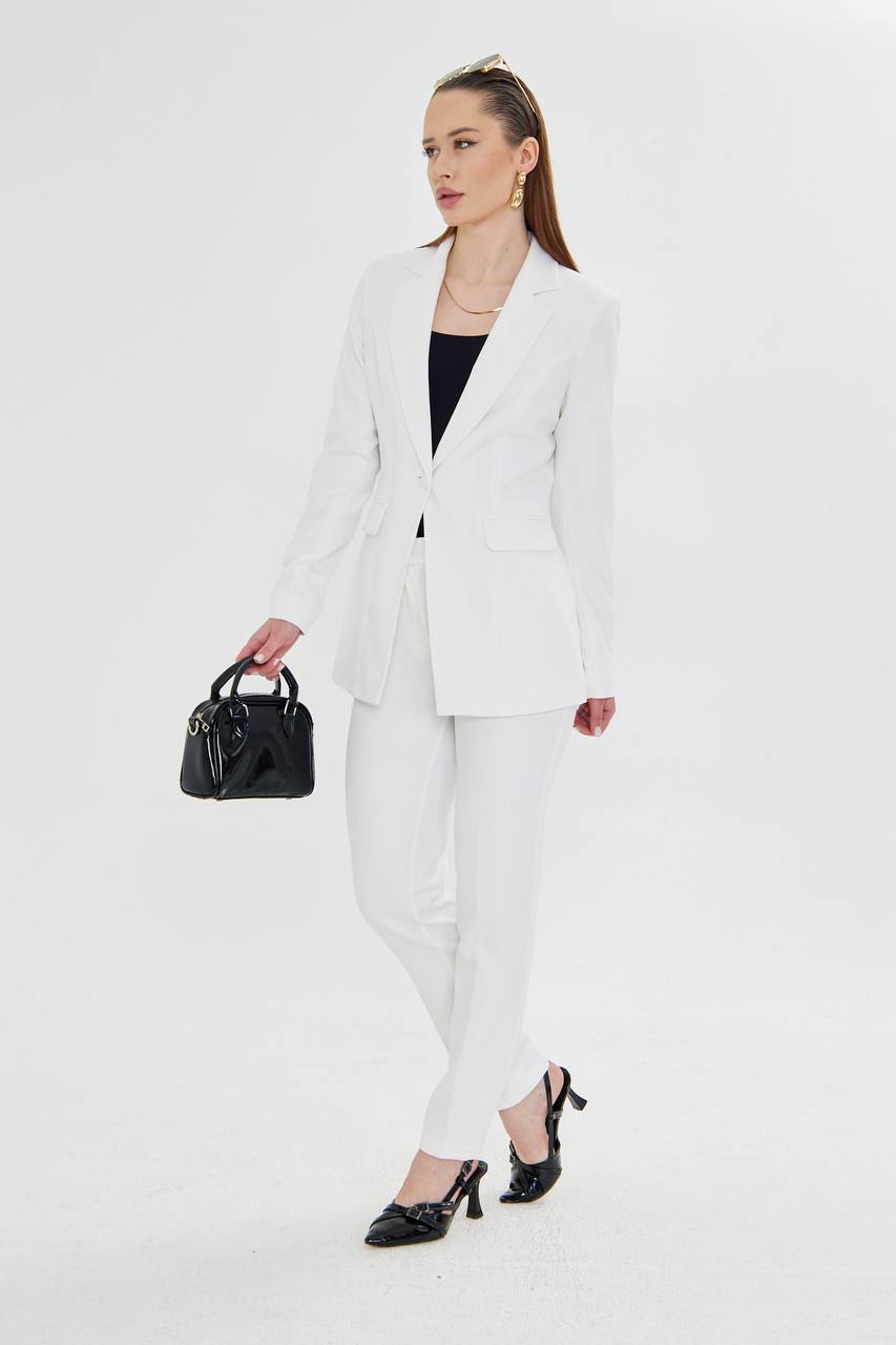 Woman in a white suit holding a black handbag on a white background