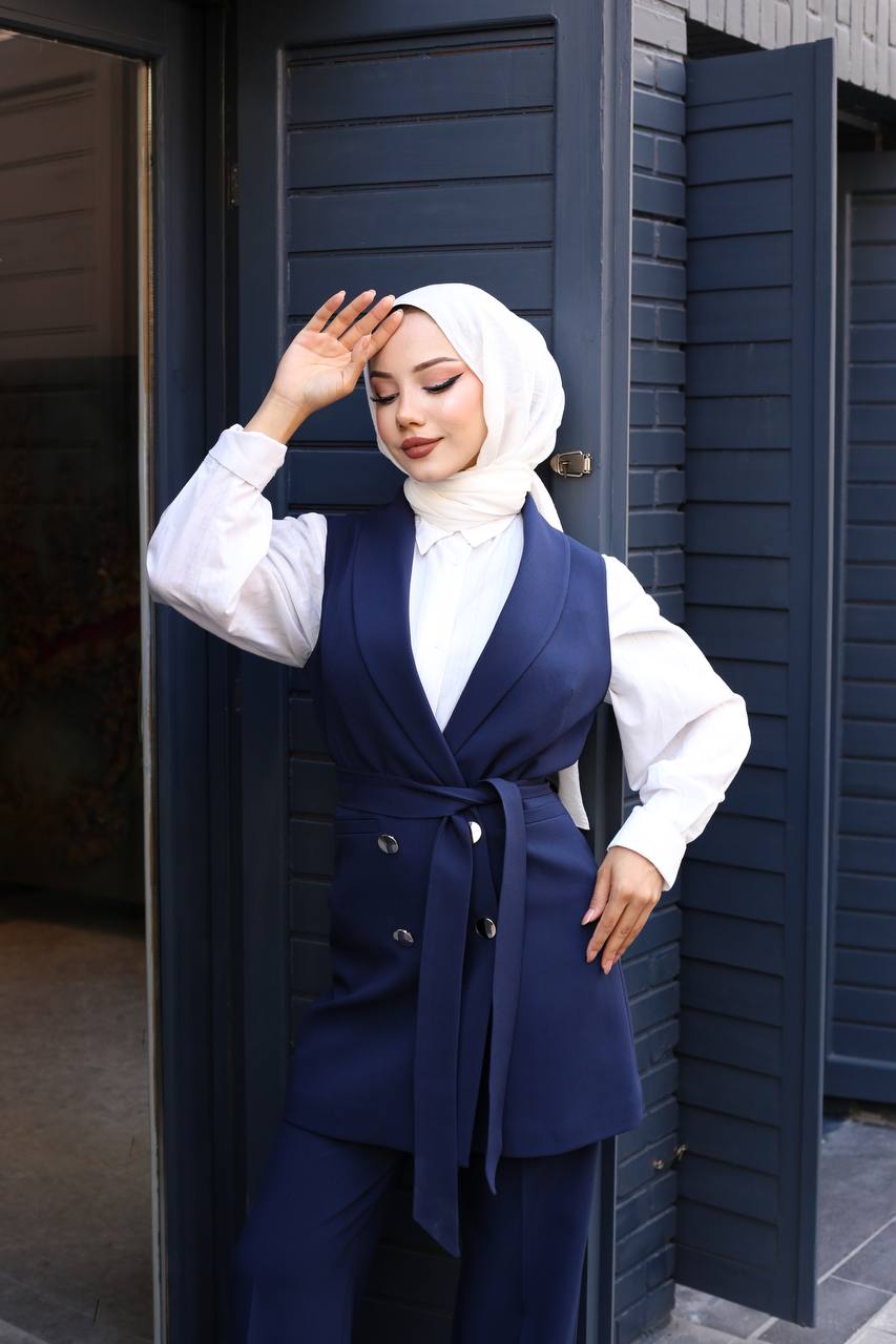 Woman wearing a navy blue outfit with a white hijab standing in front of a dark blue door.