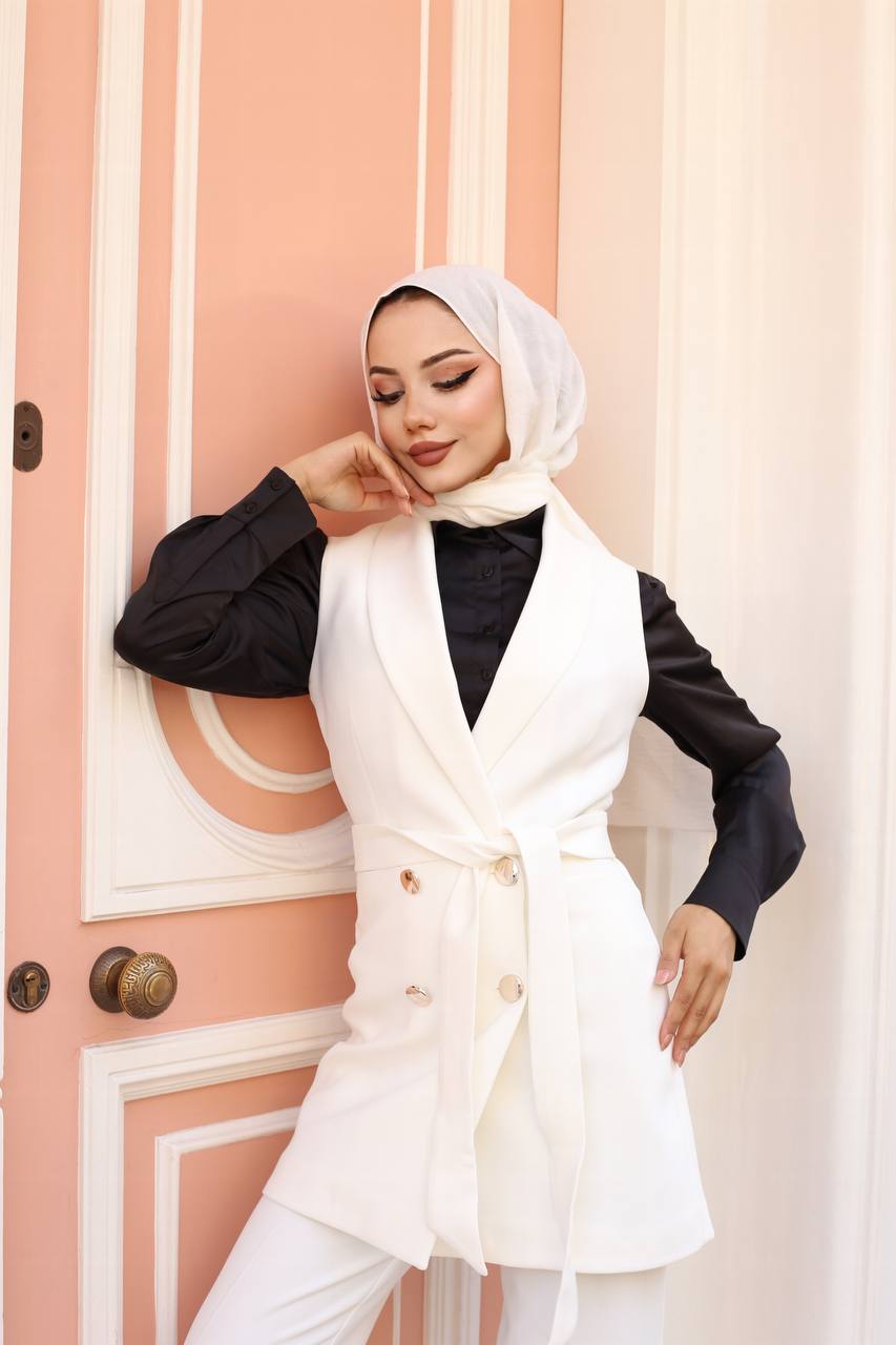 Woman wearing a white blazer over a black top in front of a pink door.