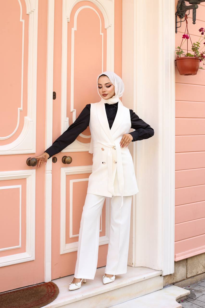 Woman in a white outfit standing in front of a pink door.