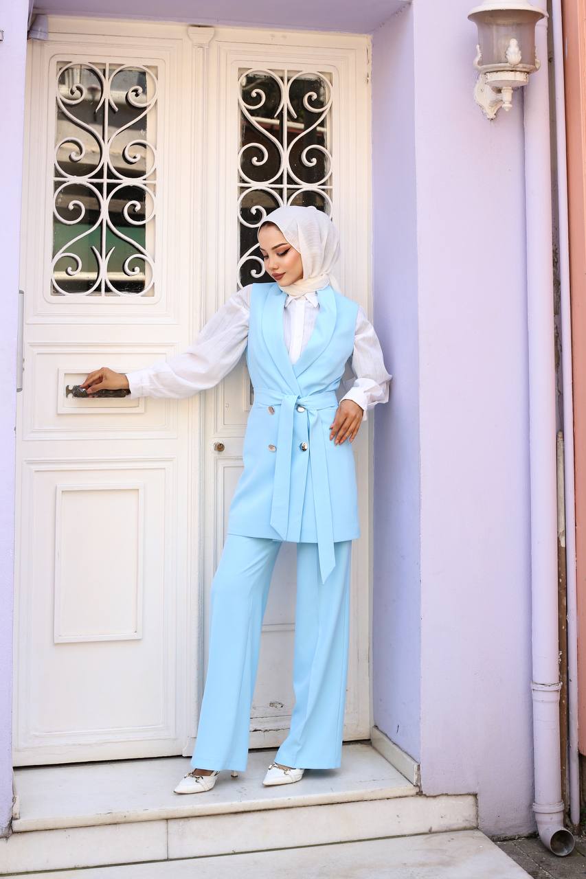 Woman in a light blue outfit standing in front of a white door with decorative ironwork.