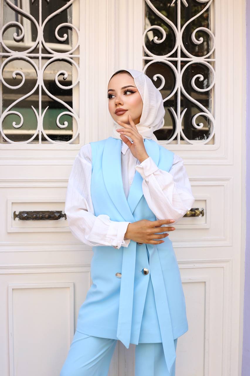 Woman wearing a light blue vest over a white shirt in front of a decorative door.