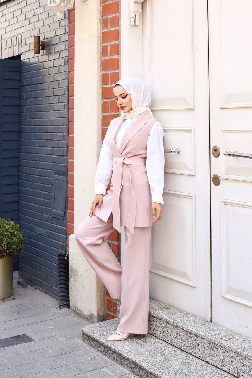 Woman in a pink outfit standing on a sidewalk next to a building entrance.