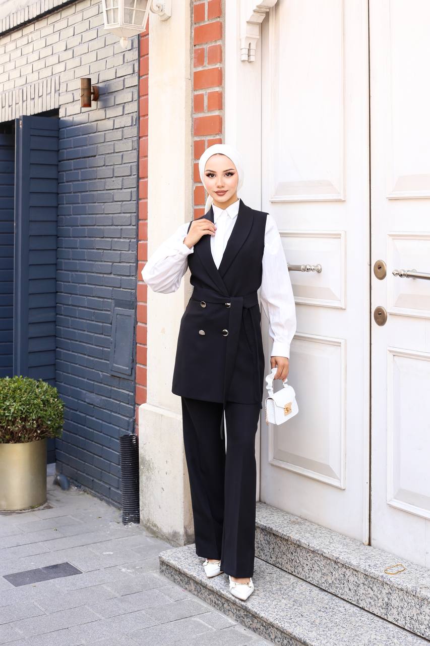 Woman in a black vest and white shirt standing outside a building.