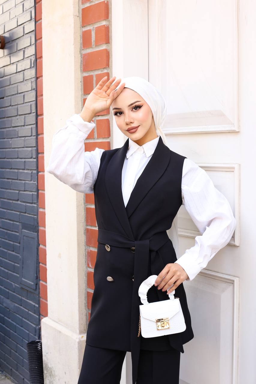 Woman in a black vest and white shirt standing against a brick wall.