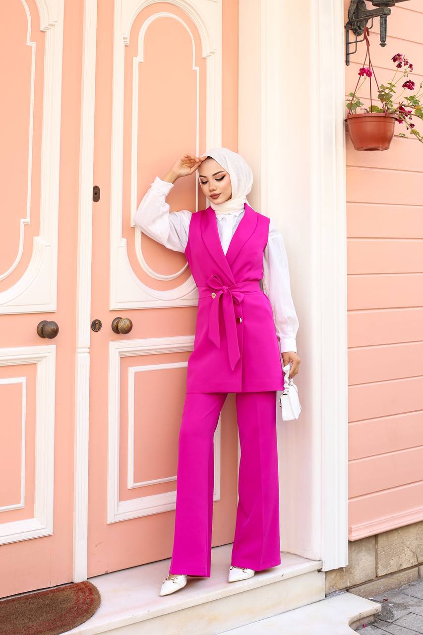 Person wearing a bright pink outfit with a white top and matching pants, standing in front of a pink door.