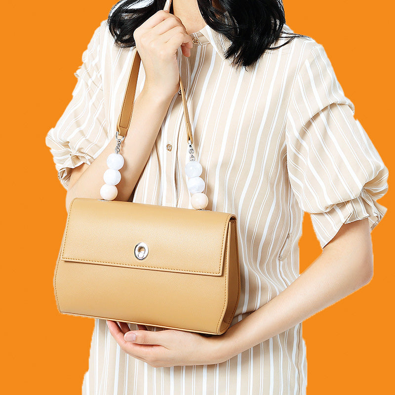 Person holding a tan handbag with white beads against an orange background