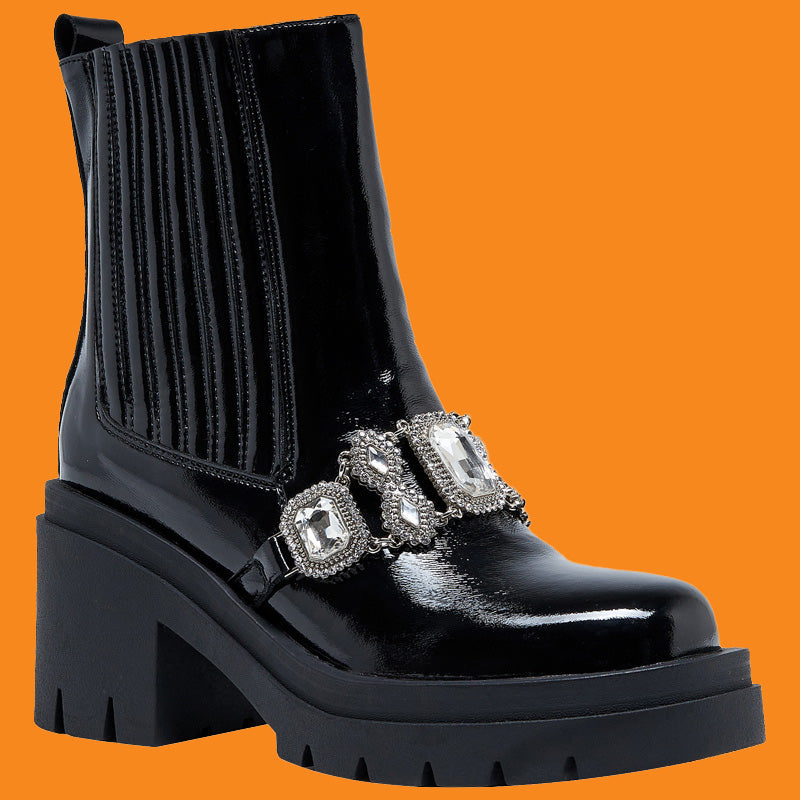 Black patent leather boot with decorative straps on an orange background