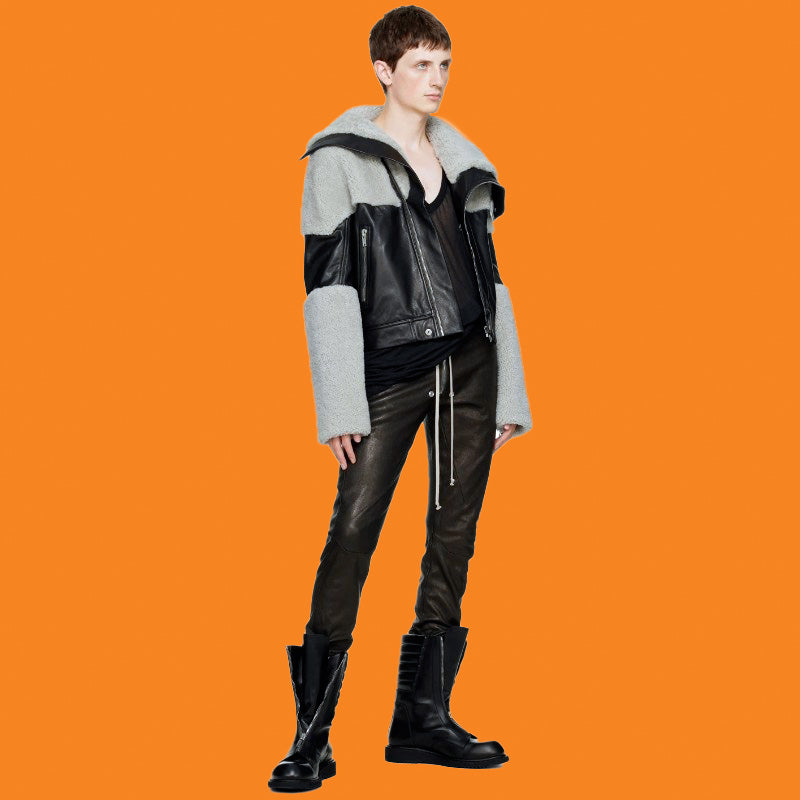 Person wearing a gray and black jacket with leather elements on an orange background
