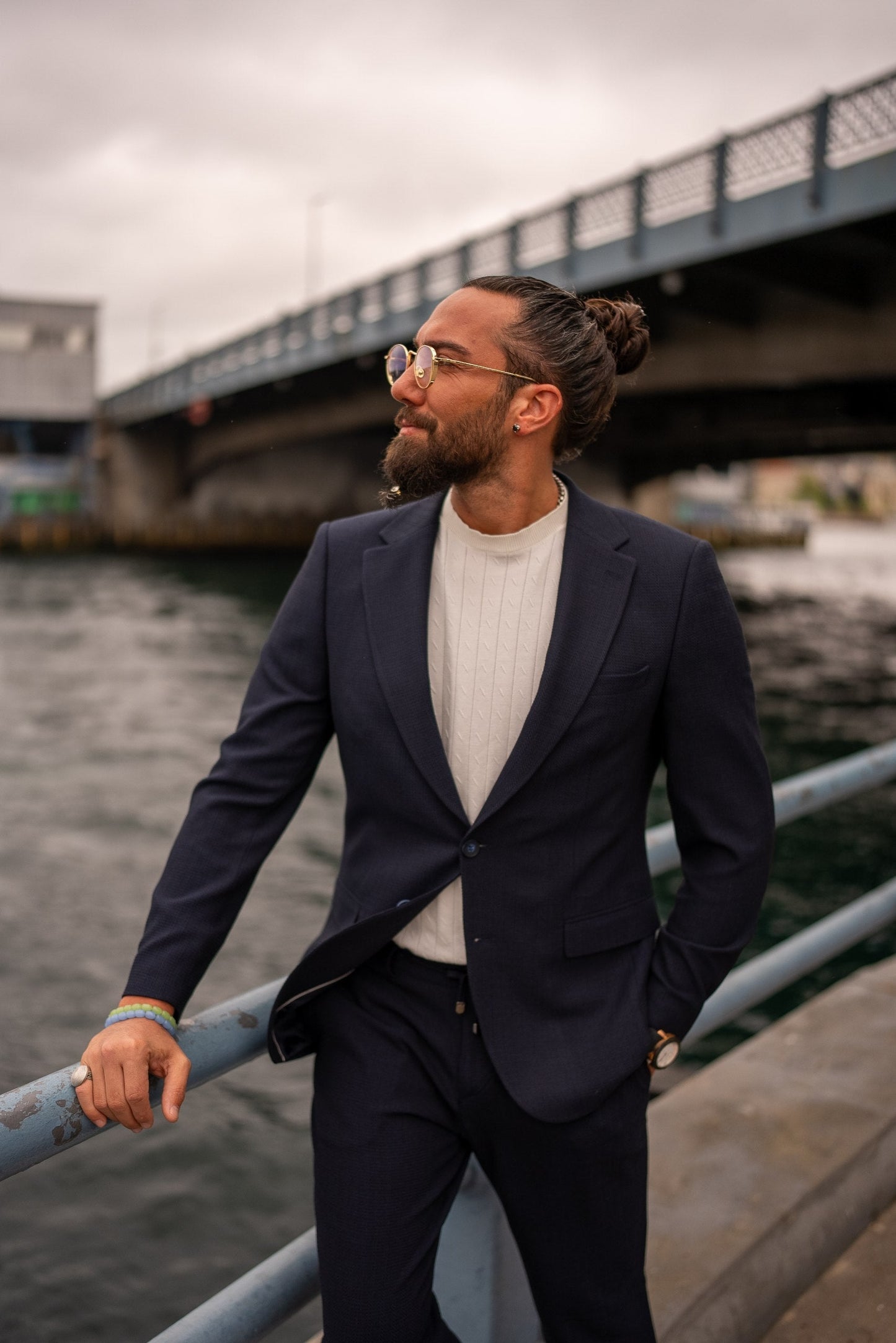 Man in a suit standing by a waterfront with a bridge in the background