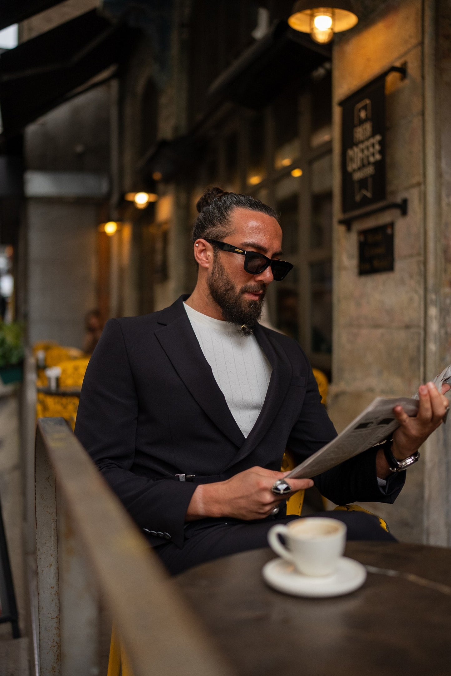 Man in a suit reading a menu at an outdoor cafe.