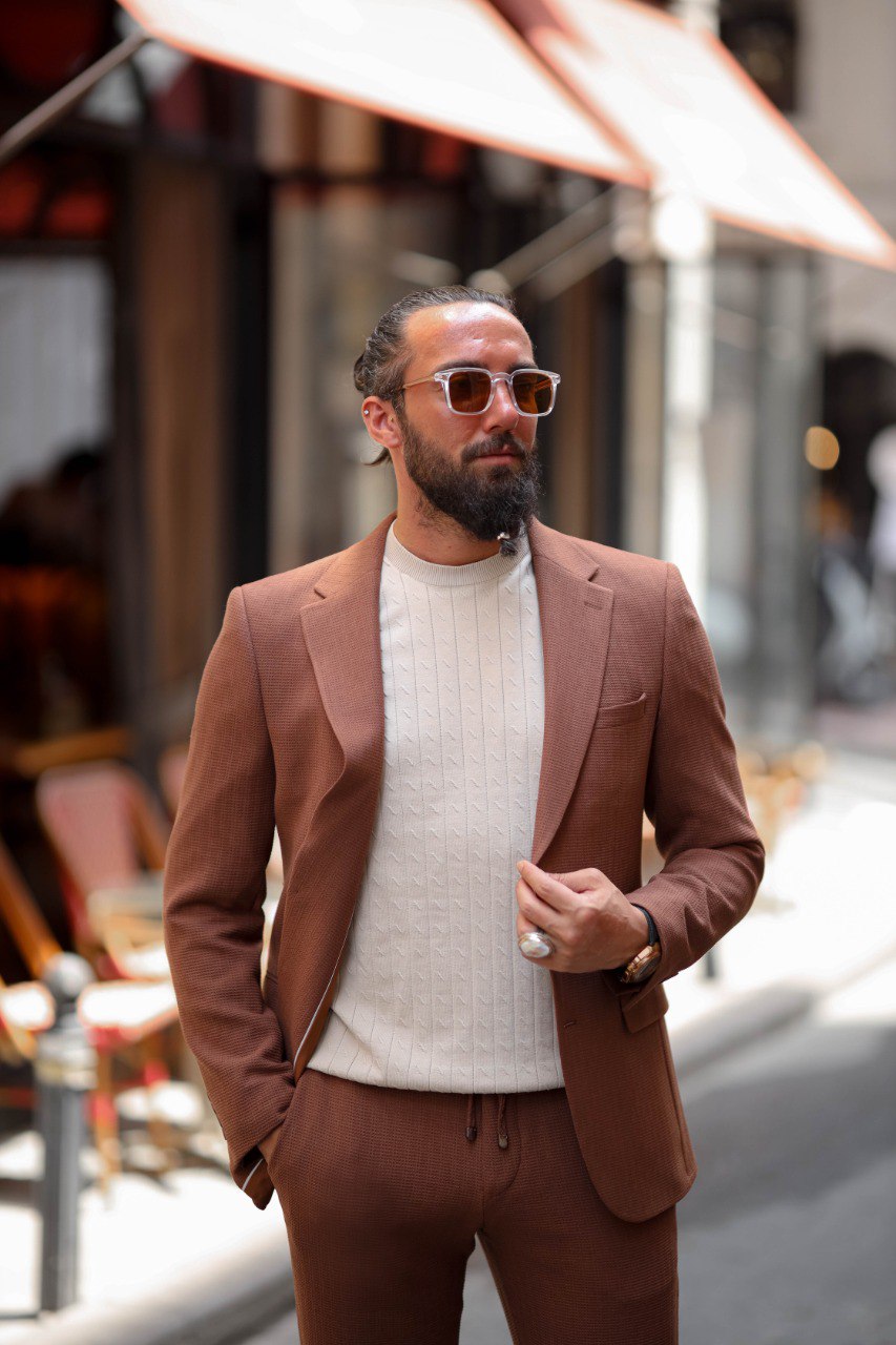 Man wearing a brown suit and white sweater on a city street.