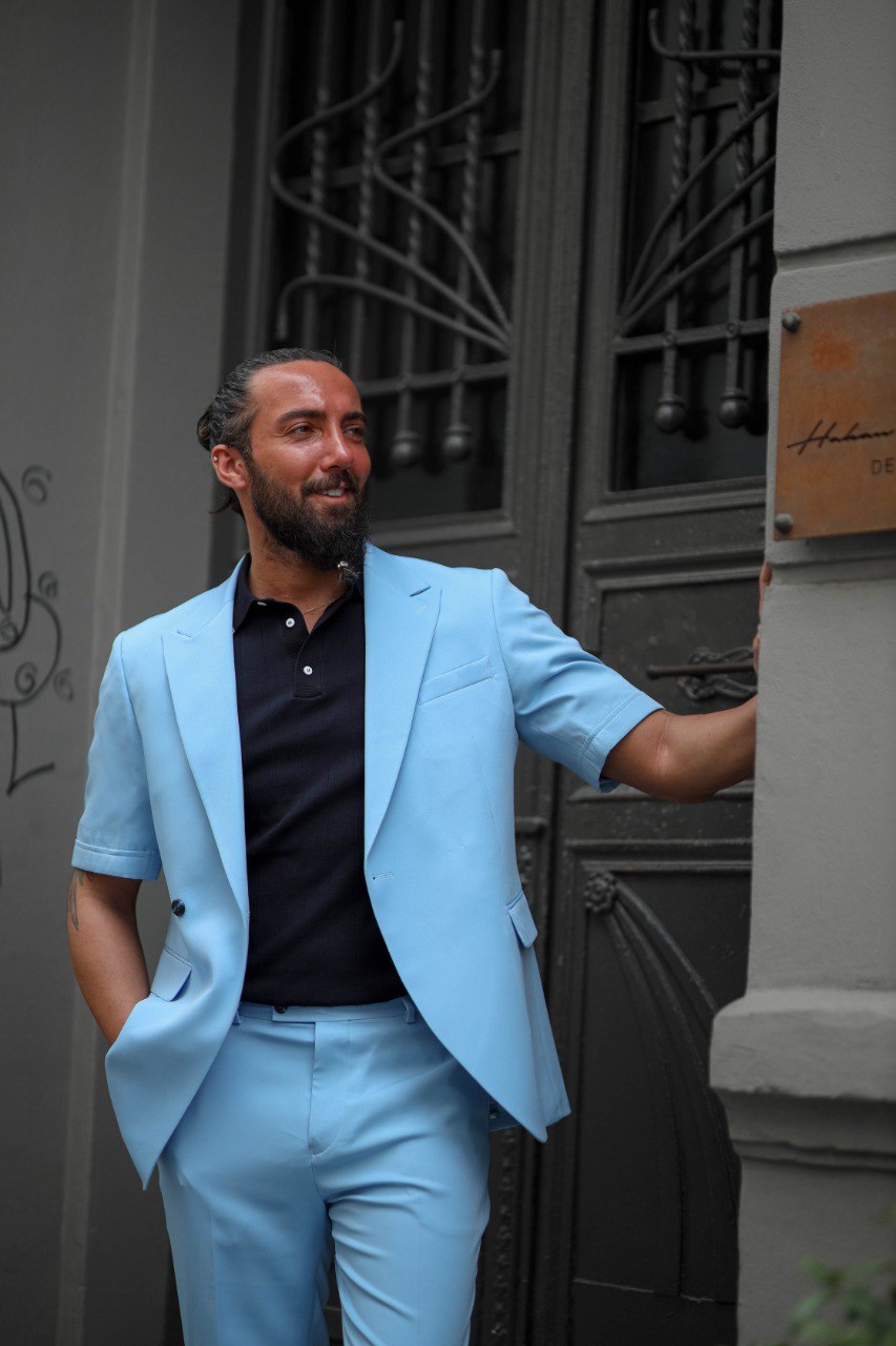 Man wearing a light blue suit standing against a building entrance.