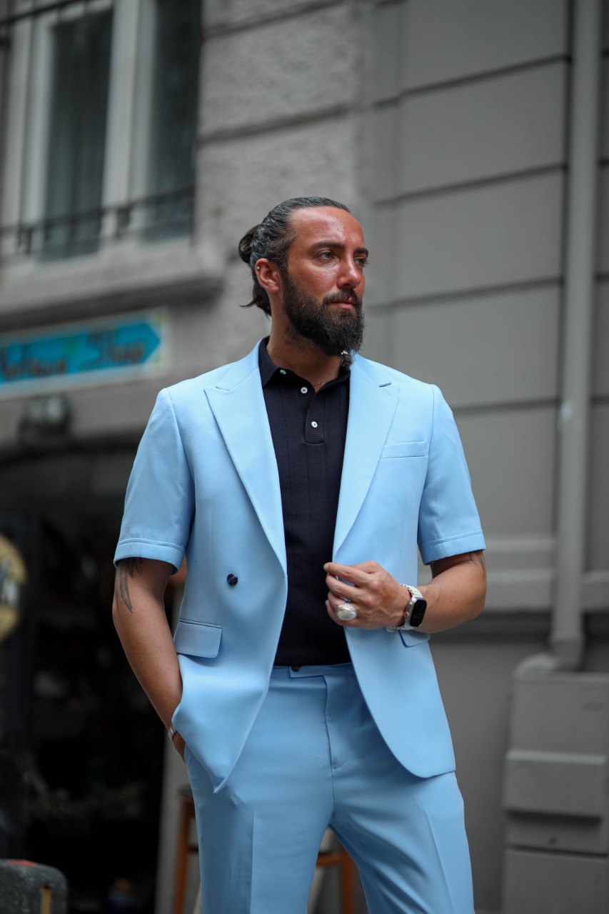 Man wearing a light blue suit standing against a building.
